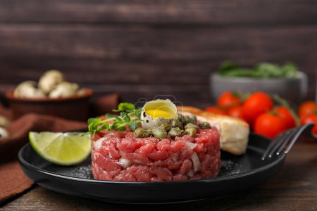 Photo for Tasty beef steak tartare served with quail egg and other accompaniments on wooden table - Royalty Free Image