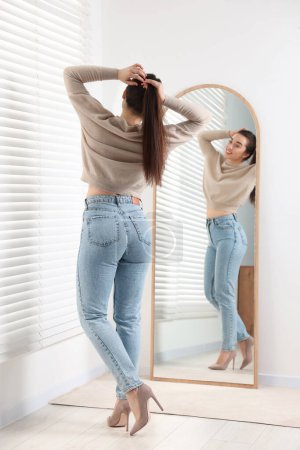 Young woman in stylish jeans near mirror indoors Poster 648112120