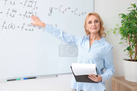 Professor with clipboard giving lecture near whiteboard in classroom