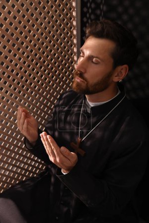 Foto de Sacerdote católico en sotana orando a Dios en cabina confesional - Imagen libre de derechos