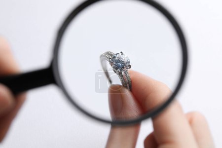 Jeweler examining diamond ring with magnifying glass at white background, closeup