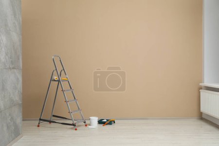 Metallic folding ladder and painting tools near beige wall indoors, space for text