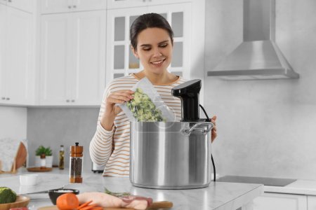 Photo for Woman putting vacuum packed broccoli into pot with sous vide cooker in kitchen. Thermal immersion circulator - Royalty Free Image