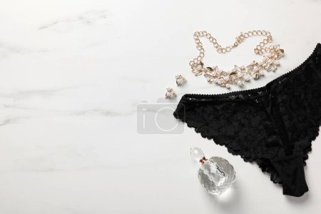 Elegante schwarze Damenunterwäsche, Accessoires und Parfüm auf weißem Marmorhintergrund, flach gelegt. Raum für Text