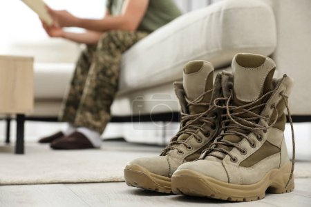 Foto de Soldado con revista en sofá en la sala de estar, se centran en un par de botas de combate. Servicio militar - Imagen libre de derechos