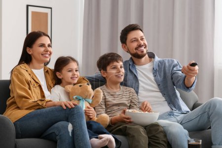 Foto de Familia feliz viendo la televisión en casa. Padre cambiando canales con control remoto - Imagen libre de derechos