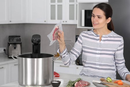 Woman putting vacuum packed meat into pot with sous vide cooker in kitchen. Thermal immersion circulator