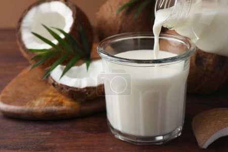 Téléchargez les photos : Verser du délicieux lait de coco dans du verre sur une table en bois - en image libre de droit