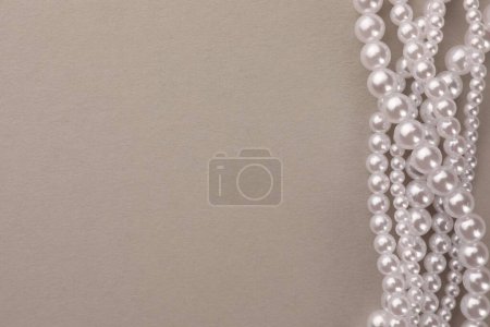 Elegant pearl necklace on beige background, top view. Space for text