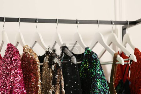 Clothing rack with colorful sequin party dresses on hangers near white wall indoors, closeup