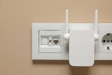Photo for Wireless Wi-Fi repeater in power socket on beige wall - Royalty Free Image