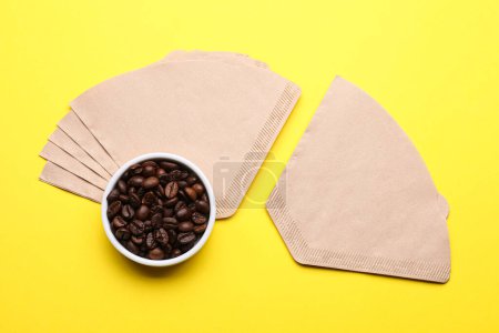Paper coffee filters and beans on yellow background, flat lay