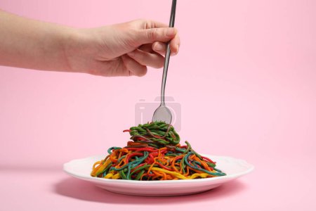 Photo for Woman eating delicious spaghetti painted with different food colorings on pink background, closeup - Royalty Free Image
