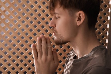 Man praying during confession near wooden window in booth, closeup