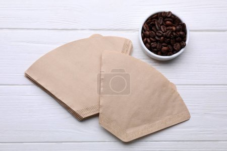 Paper coffee filters and beans on white wooden table, flat lay