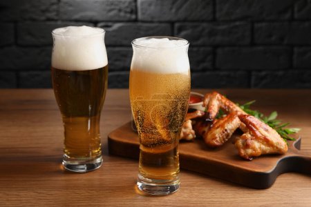 Téléchargez les photos : Verres à bière et délicieuses ailes de poulet cuites au four sur table en bois - en image libre de droit