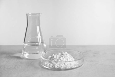 Petri dish with calcium carbonate powder and laboratory flask on light grey table. Space for text