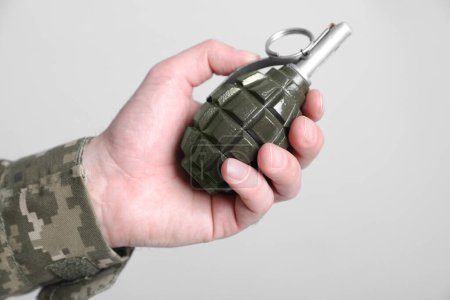 Żołnierz trzymający granat na jasnoszarym tle, zbliżenie. Służba wojskowa