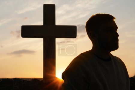 Photo for Atheism. Silhouette of man turned away from Christian cross outdoors at sunrise - Royalty Free Image