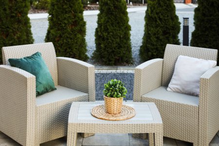 Téléchargez les photos : Beaux meubles de jardin en rotin, oreillers doux et plantes d'intérieur en plein air - en image libre de droit