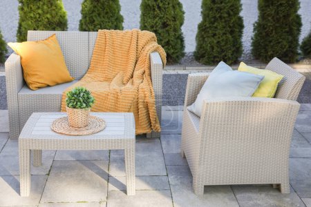Beautiful rattan garden furniture, soft pillows, blanket and houseplant outdoors