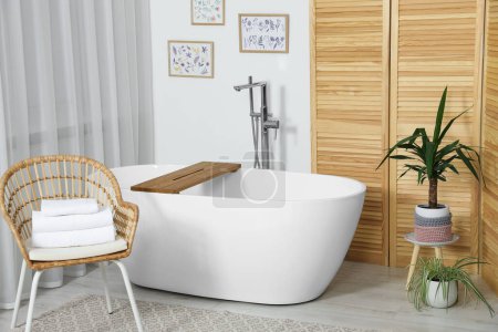 Photo for Stylish white tub and chair with towels in bathroom. Interior design - Royalty Free Image