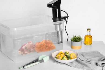 Photo for Thermal immersion circulator and vacuum packed meat in box on white wooden table. Sous vide cooking - Royalty Free Image