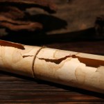 Scroll of old parchment paper on wooden table, closeup