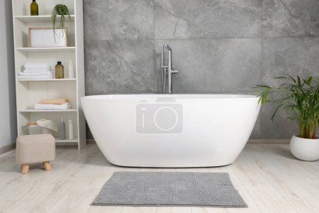 Foto de Elegante baño interior con bañera de cerámica, productos de cuidado y toallas en el gabinete - Imagen libre de derechos