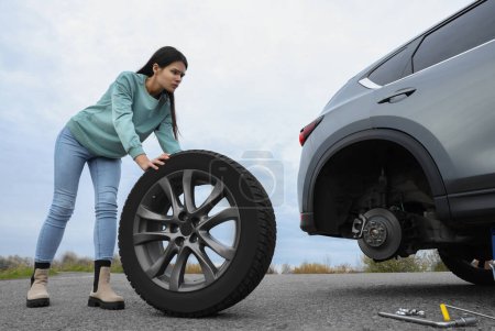 Young woman changing tire of car on roadside