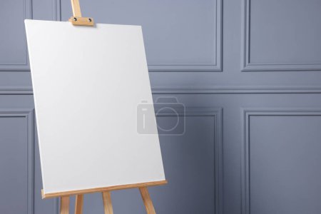Photo for Wooden easel with blank canvas near grey wall indoors, closeup. Space for text - Royalty Free Image