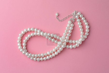 Elegant necklace with pearls on pink background, top view