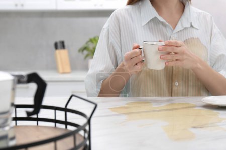 Photo for Woman with spilled coffee over her shirt at marble table in kitchen, closeup - Royalty Free Image