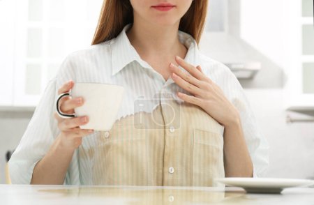 Photo for Woman with spilled coffee over her shirt at table in kitchen, closeup - Royalty Free Image