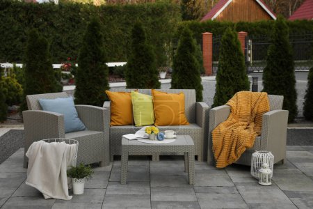 Beautiful rattan garden furniture, soft pillows and different decor elements in backyard