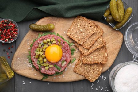 Photo for Tasty beef steak tartare served with yolk, pickled cucumber and other accompaniments on grey wooden table, flat lay - Royalty Free Image