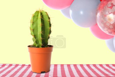 Photo for Balloons over table with cactus against pastel yellow background - Royalty Free Image