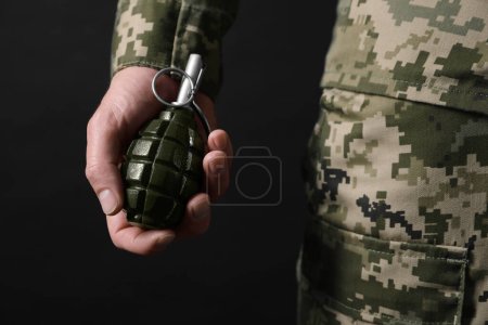 Soldier holding hand grenade on black background, closeup. Military service