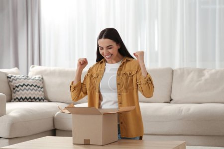 Photo for Emotional young woman opening parcel at home. Internet shopping - Royalty Free Image