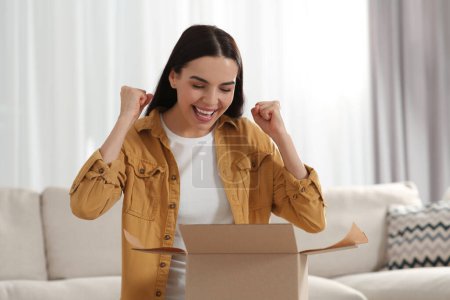 Photo for Emotional young woman opening parcel at home. Internet shopping - Royalty Free Image