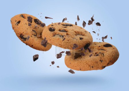 Foto de Sabrosas galletas de chispas de chocolate cayendo sobre fondo azul claro - Imagen libre de derechos