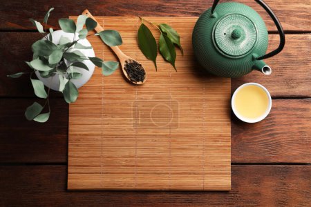 Photo for Flat lay composition with bamboo mat, dry tea leaves and teapot on wooden table, space for text - Royalty Free Image
