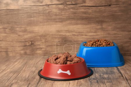 Photo for Dry and wet pet food in feeding bowls on wooden floor, space for text - Royalty Free Image