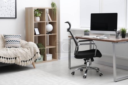 Gemütliche Arbeitsfläche mit Computer am Schreibtisch, stilvollen Möbeln und Topfpflanzen zu Hause