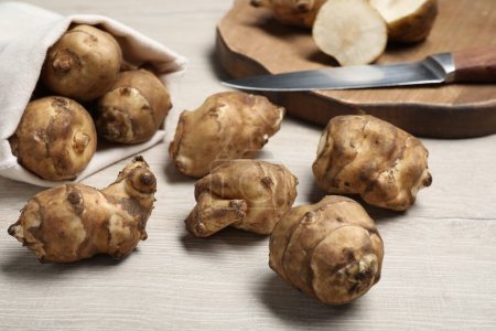 Bag and many Jerusalem artichokes with knife on white wooden table