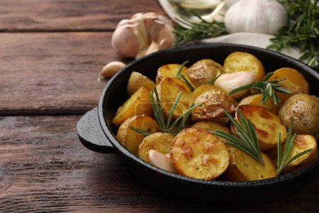 Téléchargez les photos : Délicieuses pommes de terre cuites au four avec romarin dans une poêle sur une table en bois. Espace pour le texte - en image libre de droit