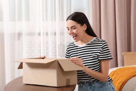 Emotionale junge Frau beim Paketöffnen zu Hause. Internet-Einkauf