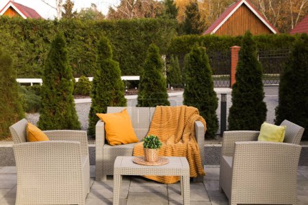 Schöne Gartenmöbel aus Rattan, weiche Kissen, Decke und Zimmerpflanze im Garten