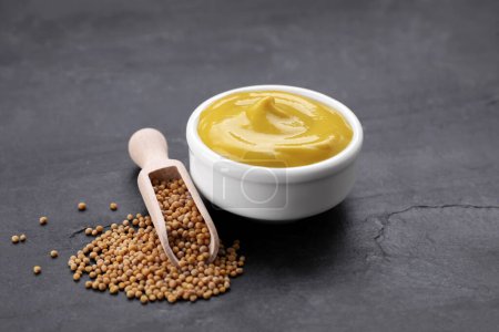 Bol de moutarde délicieuse et cuillère avec des graines sur table texturée noire
