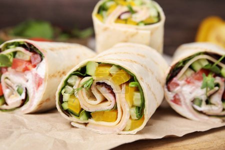 Delicious sandwich wraps with fresh vegetables on wooden board, closeup